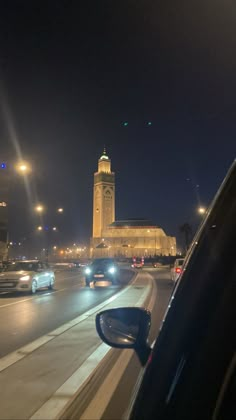 cars driving down the road in front of a tall clock tower at night with lights on