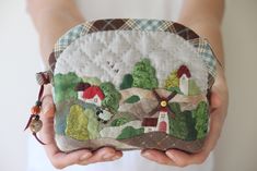 a person holding a small purse with houses on the front and trees on the back