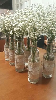 white flowers are in glass vases on a wooden table with string wrapped around them