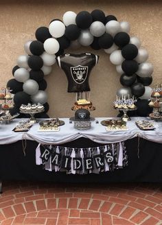 a table topped with balloons and black and white desserts next to a football helmet