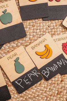 several wooden signs with different fruits and vegetables on them sitting on a woven tablecloth