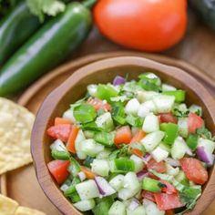 a wooden bowl filled with cucumber, tomato and onion salad next to tortilla chips