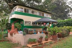 a green and white bus parked in front of a house with potted plants on the side