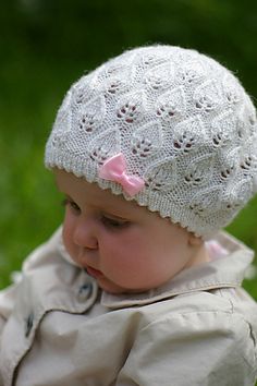 a baby girl wearing a white hat with pink bows on it's head and looking down