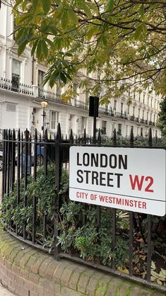 a street sign in front of an iron fence and trees on the side of the road