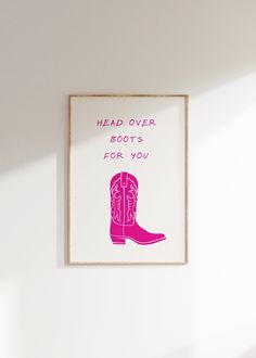 a pink cowboy boot with the words head over boots for you on it hanging above a white wall