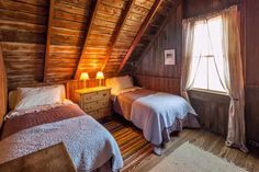 two beds in a small room with wooden walls and flooring on either side of the bed