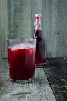 two glasses filled with liquid sitting on top of a wooden table next to a bottle