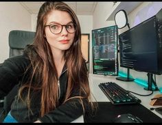 a woman wearing glasses sitting in front of a computer desk with a keyboard and monitor