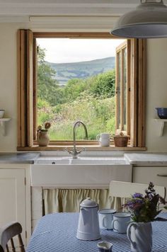 a kitchen with a sink, window and table in front of an open window that looks out onto the countryside