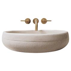 a white sink with two brass faucets on it's sides and a round bowl