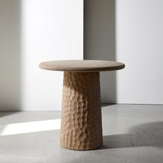 a round wooden table sitting on top of a cement floor next to a wall and window