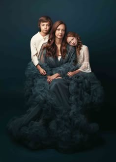 three people sitting on top of each other wearing black dresses and posing for the camera