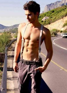 a shirtless man walking down the street with his hand in his pocket and no shirt on