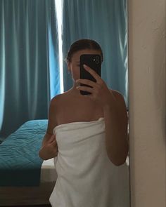 a woman taking a selfie in front of a mirror wearing a towel and holding a cell phone