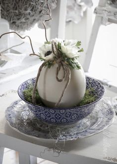 a white pumpkin sitting on top of a blue and white plate covered in grass with flowers