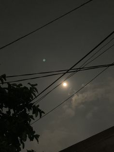 the moon shines brightly in the dark sky above power lines and telephone wires on a cloudy night