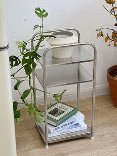 a plant and some books on a metal shelf next to a white wall with a potted plant