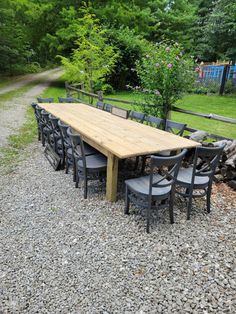 a wooden table surrounded by black chairs on gravel