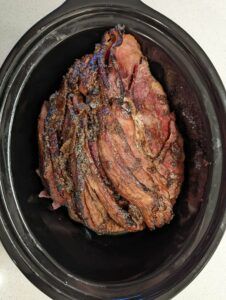 a large piece of meat in a black crock pot on a white counter top