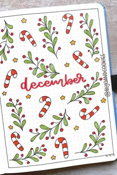 an open christmas card with candy canes and holly branches on it, next to a pen