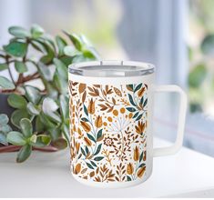 a white coffee mug sitting on top of a table next to a potted plant