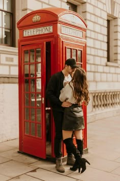 a man and woman kissing in front of a red phone booth