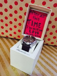 a white box with a watch inside it on a table next to a red polka dot wall