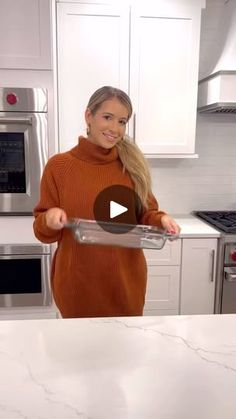 a woman in a kitchen holding a pan with food on it and smiling at the camera