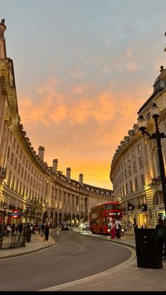 the sun is setting in an old european city with tall buildings and people walking on the street