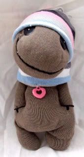 a brown stuffed animal with a pink button on it's collar and hat sitting on a white sheet