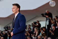 a man in a blue suit and black tie standing on a red carpet with cameras around him