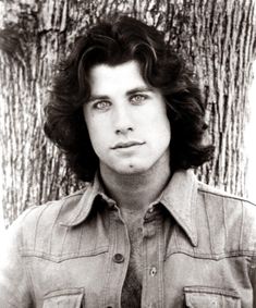 a black and white photo of a man with long hair wearing a denim shirt in front of a tree