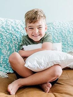 a young boy sitting on top of a bed with pillows in front of his face