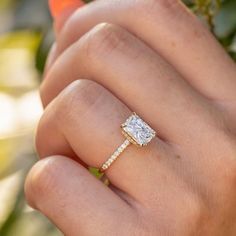 a woman's hand with a diamond ring on her finger and an orange flower in the background