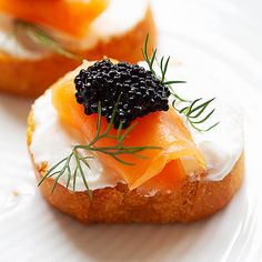 a white plate topped with two small cakes covered in cream cheese and black cavia