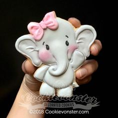 an elephant cookie is being held in someone's hand with a pink bow on its head