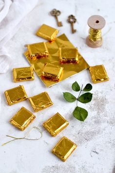 several pieces of gold foil next to a sprig of green leaves and thread