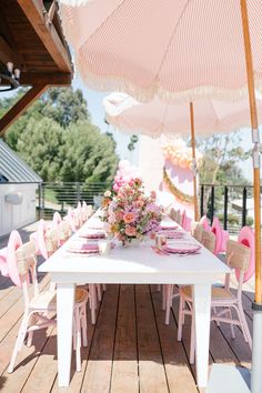 a white table with pink chairs and an umbrella over it on a wooden deck outside