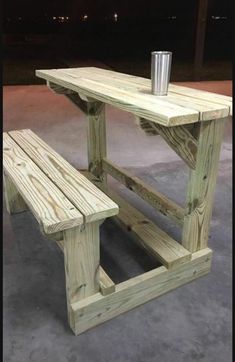 a wooden table and bench with a cup on the top, sitting outside at night