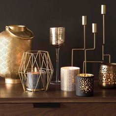 candles are lined up on a table next to a gold vase and candle holder,