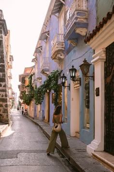 a woman is walking down the street in front of some blue and white buildings with balconies