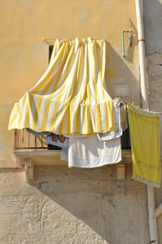 clothes hanging out to dry on a line outside an old building with yellow and white striped curtains