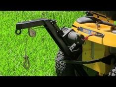 a yellow lawn mower sitting on top of a green grass covered field next to a metal hook