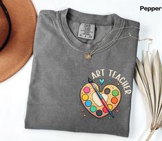 a t - shirt that says art teacher on it next to a hat and feathers