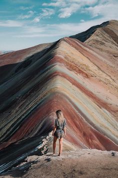 a woman standing on top of a hill next to a rainbow colored mountain range in peru