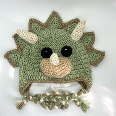 a crocheted green hat with black eyes and horns on the front, made to look like a dinosaur