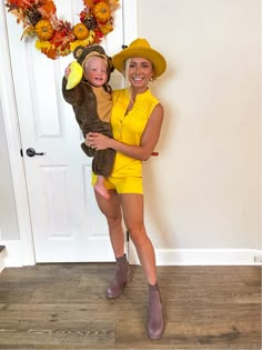 a woman in a yellow dress holding a baby wearing a bear costume and standing next to a door