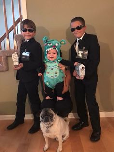 three men in suits and one is holding a small child while the dog stands next to them