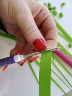 a person is cutting up some green paper with scissors and glue on it's fingers